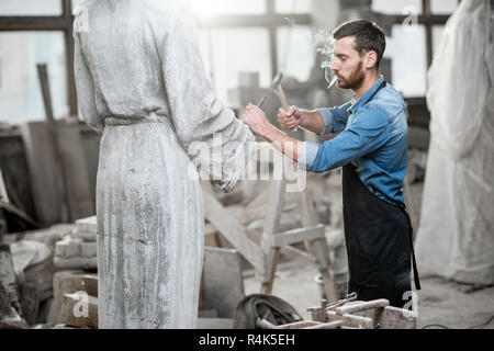 Stattliche rauchen Bildhauer schlagende Stein Skulptur mit Hammer und Meißel im Studio Stockfoto