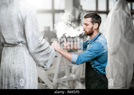 Stattliche rauchen Bildhauer schlagende Stein Skulptur mit Hammer und Meißel im Studio Stockfoto