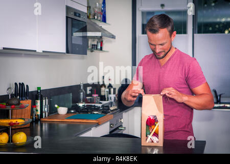 Junger Mann öffnet sich ein Paket von frischen Zutaten ein gesundes Abendessen zu machen Stockfoto