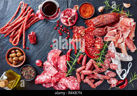 Tapas Auswahl. Ein Stein Schneidbrett mit Wurstwaren. Spanische Wurstwaren, jamon, chistorra, Chorizo, salchichon, ein Glas mit rotem Wein, Oliven, gra Stockfoto