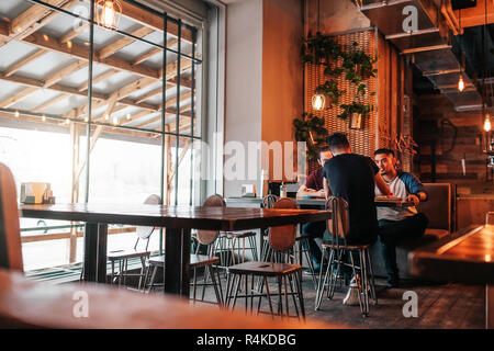 Gerne arabische junge Männer hängen in loft Café. Gruppe von gemischten Rennen die Menschen reden in der Lounge Bar. Freunde Chillen und Entspannen Stockfoto