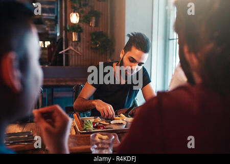 Multirassischen Freunde essen Frühstück Lounge Bar. Junge arabische Männer Chat während mit leckeren Speisen und Getränken. Chillen fith besten Freunden im Pub Stockfoto