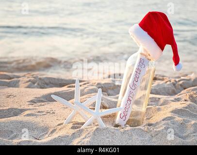 Santa Hut auf Nachricht in einer Flasche mit weißer Seestern in Sand und Weihnachtsgrüße anmelden Stockfoto