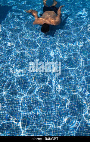 Junge, gebräunte Mann schwimmen Längen in einem Pool mit Sonne in den welligen Wasser und weg von der gefliesten Boden wider. Stockfoto