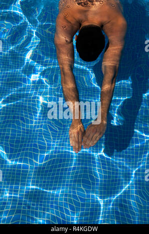 Junge, gebräunte Mann schwimmen Längen in einem Pool mit Sonne in den welligen Wasser und weg von der gefliesten Boden wider. Stockfoto