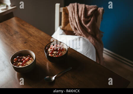 Zwei Schalen mit Porridge mit Trauben auf einen hölzernen Tisch mit Stuhl und Decke im Hintergrund Stockfoto