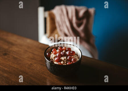 Zwei Schalen mit Porridge mit Trauben auf einen hölzernen Tisch mit Stuhl und Decke im Hintergrund Stockfoto