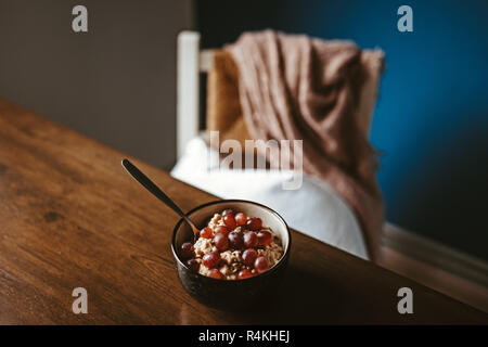 Zwei Schalen mit Porridge mit Trauben auf einen hölzernen Tisch mit Stuhl und Decke im Hintergrund Stockfoto