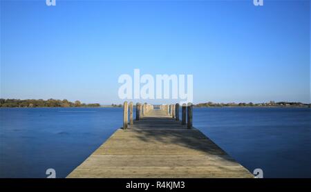 Eine leere Pier befindet sich auf ruhigen blauen Wasser unter einem wolkenlosen blauen Himmel Stockfoto