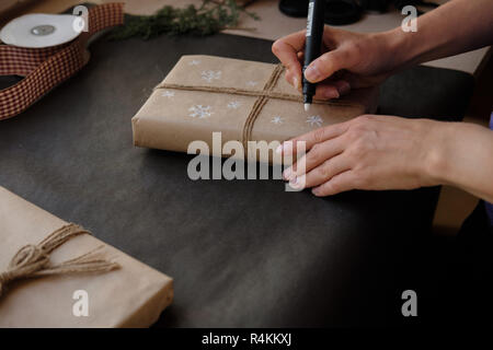 Frau Zeichnung auf Papier Schneeflocken Paket Weihnachten, Geschenk auf schwarzem Hintergrund. Weibliche Hände malen auf Geschenke für Winterurlaub. Weihnachten, Ne Stockfoto