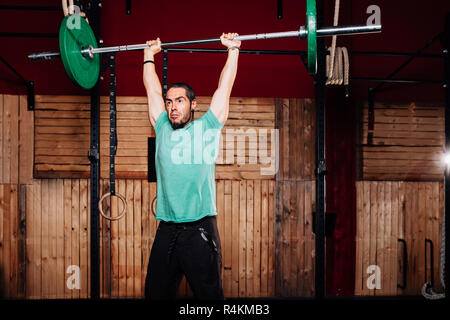 Athletischen jungen Mann dabei einige weightlifting Übungen mit grünem T-Shirt Stockfoto