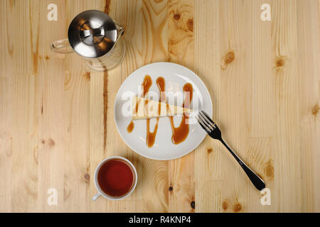 Platte mit Käsekuchen unter Karamell-Sauce, eine Tasse Tee und eine Teekanne Stand auf einem hölzernen Leuchttisch. Ansicht von oben Stockfoto