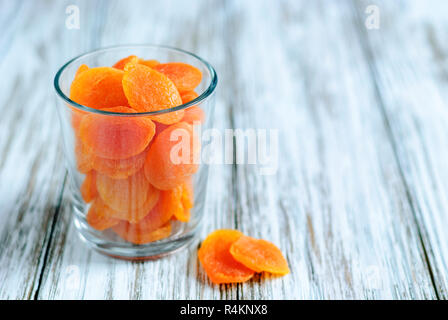 Closeup Schuß aus transparentem Glas gefüllt mit Haufen Sweet Orange getrocknete Aprikosen auf hölzernen Tisch Stockfoto