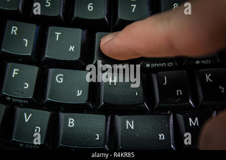 Mann, das Schreiben auf einer Tastatur mit Buchstaben in Hebräisch und Englisch Stockfoto