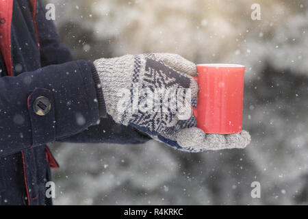 Nahaufnahme des Menschen Hände tragen wollene Handschuhe holding Tasse heißes Getränk gegen Winter Hintergrund. Stockfoto