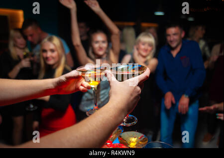 Zwei Martini Gläser in den Händen und Gruppe von glücklichen Menschen. Neues Jahr oder Weihnachtsfeier Konzept. Stockfoto