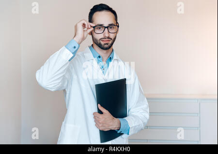 Allein Arzt in Gläsern steht in seiner privaten, weißen Arzneischrank Stockfoto