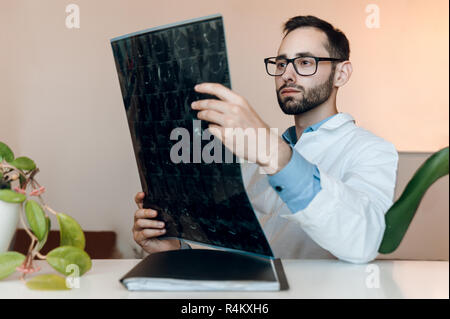 Junger Arzt sitzt in Kabinett und Blick auf Magnetic Resonance Imaging geschossen von kniegelenk. Meniskus Verletzungen mrt Röntgen Stockfoto