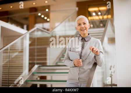 Portrait von Senior geschäftsfrau stehen in modernen Büro- und Holding digital Tablet Stockfoto
