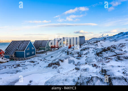 Gelb, blau, rot und grün Inuit Häuser entlang der Straße von Schnee mit Felslandschaft im Vordergrund und die Berge im Hintergrund, Stadt Nuuk, Grönland Stockfoto