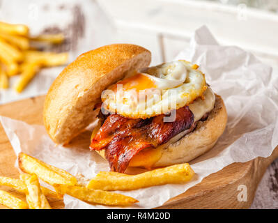 Speck und Ei Burger serviert auf einem Schneidebrett mit hausgemachten Pommes frites. Stockfoto