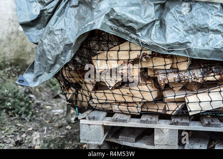 Ein großer woodpile vieler geschnitten natürliche Brennholz Birke trocknen außerhalb auf einem ländlichen Palette mit einem rauhen Plane in der Landschaft abgedeckt Stockfoto