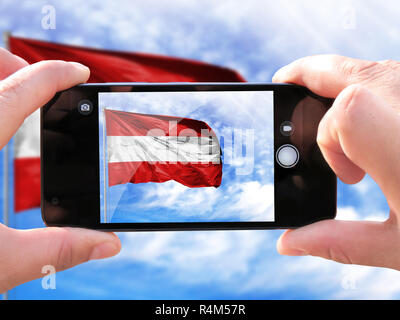 Das Konzept des Tourismus und Reisen. Die Hände der Männer machen ein Foto vom Telefon. Schießen aus dem Smartphone Flagge von Österreich auf dem Fahnenmast gegen Stockfoto