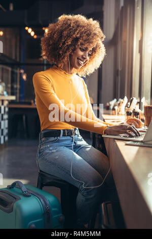 Lächelnd afro-amerikanische Frau im Coffeeshop Arbeiten am Laptop sitzen, während Sie Musik hören. Weibliche Reisende im Urlaub tun ein Video Stockfoto