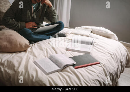 Student Studium hart sitzen auf dem Bett mit Laptop und Bücher auf dem Bett. Schüler mit Laptop sitzen und Bücher, die auf dem Bett. Stockfoto