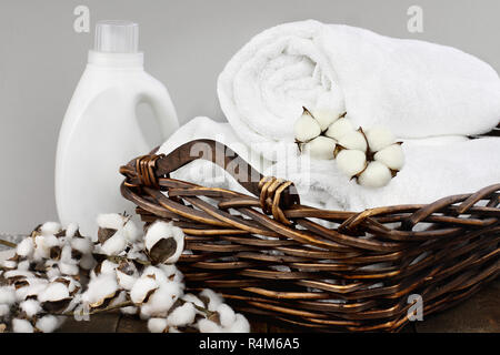 Wäsche Korb weiße flauschige Handtücher, Baumwolle, Blumen und eine Flasche flüssige Seife gegen einen unscharfen Hintergrund grau. Stockfoto