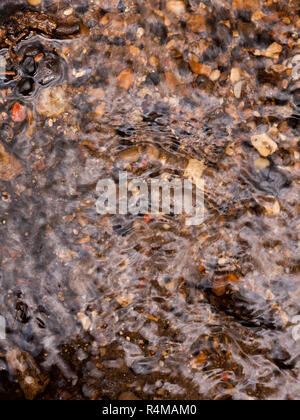 Die gerippte Oberfläche des Wassers mit bunten natürliche Kieselsteine unter der Wasseroberfläche und einige heraus Leuchtende und glitzernde wie Wasser fließt über und down stream klemmt Stockfoto