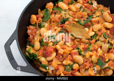 Spanische Bohnen mit Tomaten: Ein veganes Gericht mit Butterbohnen, Tomaten und Spinat, gewürzt mit geräuchertem Paprika und serviert in einer gusseisernen Pfanne Stockfoto