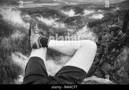 Wanderer Mann einen Rest am Berg. Männliche Beine auf scharfen Gipfel und Wanderer genießen Sie die spektakuläre Aussicht. Stockfoto