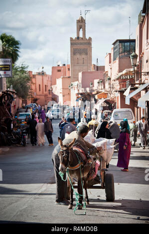 18-04-11. Marrakesch, Marokko. Fußgänger, Autos und Eseln teilen sich die Straße in der Medina, mit einem Minarett einer Moschee im Hintergrund. Foto © Simon Stockfoto