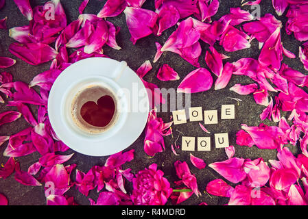 Flach Tasse Kaffee mit Herz Muster und die Nachricht Ich liebe Sie Holzblöcke mit Lila Rosa pfingstrose Blütenblätter auf Schwarz geschrieben backgrou Stockfoto