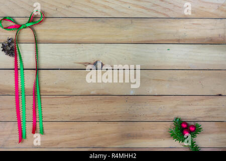 Eine rote und grüne Schleife mit Zedern Kegel auf der linken Seite mit einem roten Beere Cluster auf Balsam fir an der unteren rechten Ecke auf Holzstäbchen backgroun Stockfoto