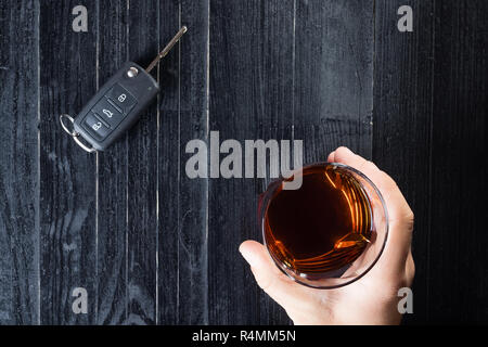 Autoschlüssel und Whiskey Alkohol in einem Glas auf schwarzen Holztisch. Trinken Sie nicht und abstraktes Konzept. Stockfoto