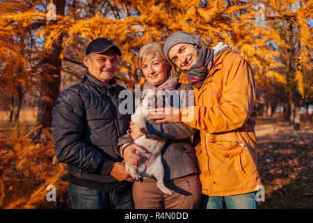 Happy Family Zeit mit Mops Hund im Herbst Park. Eltern mit ihren Sohn umarmen pet im Freien. Die Werte der Familie Stockfoto