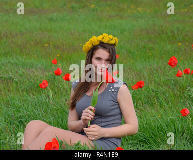 Ein Mädchen mit einem Kranz von Löwenzahn auf dem Kopf. Schönen Fee junge Mädchen in einem Feld zwischen den Blumen Tulpen. Stockfoto