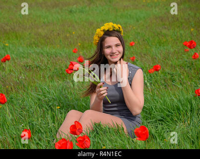 Ein Mädchen mit einem Kranz von Löwenzahn auf dem Kopf. Schönen Fee junge Mädchen in einem Feld zwischen den Blumen Tulpen. Stockfoto