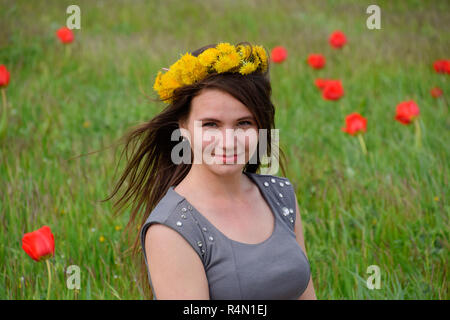 Ein Mädchen mit einem Kranz von Löwenzahn auf dem Kopf. Schönen Fee junge Mädchen in einem Feld zwischen den Blumen Tulpen. Stockfoto