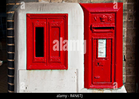 Ein an der Wand montierter Viktorianischer Briefkasten neben einem unbenutzten Typ E Stempel Automaten am Bahnhof Lowestoft in der Grafschaft Suffolk, Großbritannien Stockfoto