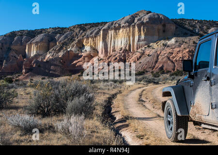 Muddy Fahrzeug mit Allradantrieb auf Schmutz der Straße in Richtung zu einer bunten Mesa in der Wüste Landschaft im Rio Chama Canyon in der Nähe von Santa Fe, New Mexico Stockfoto