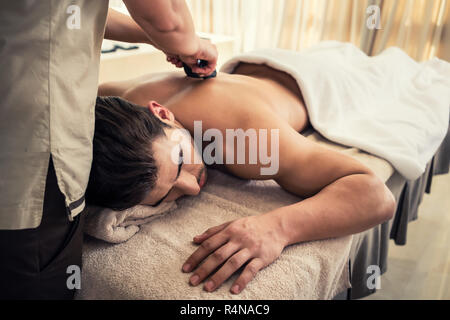 Junger Mann Entspannung während traditionelle Massage mit heißen Steinen Stockfoto