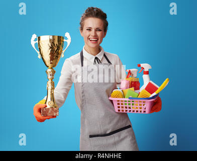 Happy Hausmädchen in Schürze mit Korb mit Wasch- und Bürsten, goldpokal vor blauem Hintergrund. Reinigung Service Nummer eins! Hausmädchen ich Stockfoto