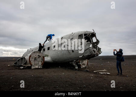 Touristen klettern Sie auf die Oberseite der Wrack eines US Navy DC-Flugzeug, das Crash an einem Strand im Süden von Island am 21. November 1973 landete. Der Ort ist abgestürzt, entweder auf Grund der niedrigen Kraftstoff oder Vereisung auf der Motoren und alle an Bord überlebten. Nach dem Absturz der Marine beraubt die Ebene der Motoren und andere wertvolle Bauteile aber nach links die wichtigsten Rumpf auf den schwarzen Sandstrand in der Nähe von Solheimasandur. Heute, zu einem großen Teil aufgrund der Geocodierung von Instagram, das Flugzeug ist ein beliebtes Ziel für Fotografen und Adventure Enthusiasten Island besuchen. Stockfoto