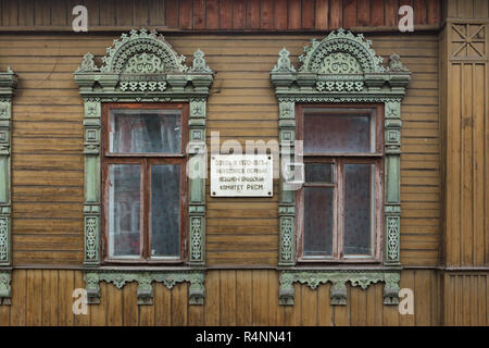 Traditionelle russische geschnitzten Fensterrahmen (nalichnik) auf dem hölzernen Haus in Ivanovo, Russland. Text in russischer Sprache auf der Gedenktafel zwischen bedeutet: Die erste Stadt und Bezirk Ausschuss Der RKSM (die russischen Jungen Kommunistischen Liga, später bekannt als die Komsomol) trafen hier in 1920-1923. Stockfoto