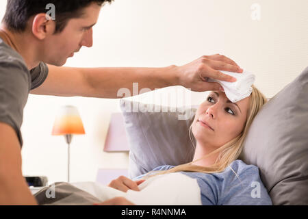 Mann mit einer Kompresse auf die Stirn von seinem Partner Stockfoto