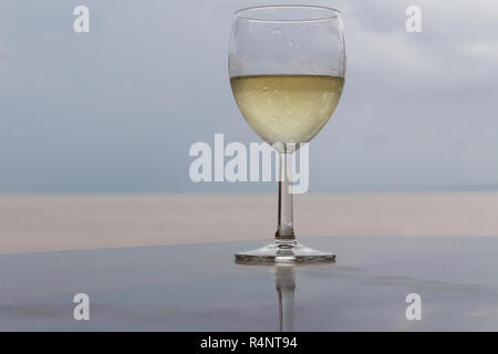 Glas Weißwein auf schwarze Balken oben mit Strand im Hintergrund Stockfoto