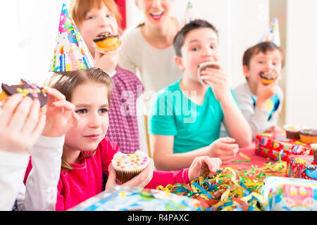 Kinder an der Geburtstagsfeier mit Muffins und Kuchen Stockfoto